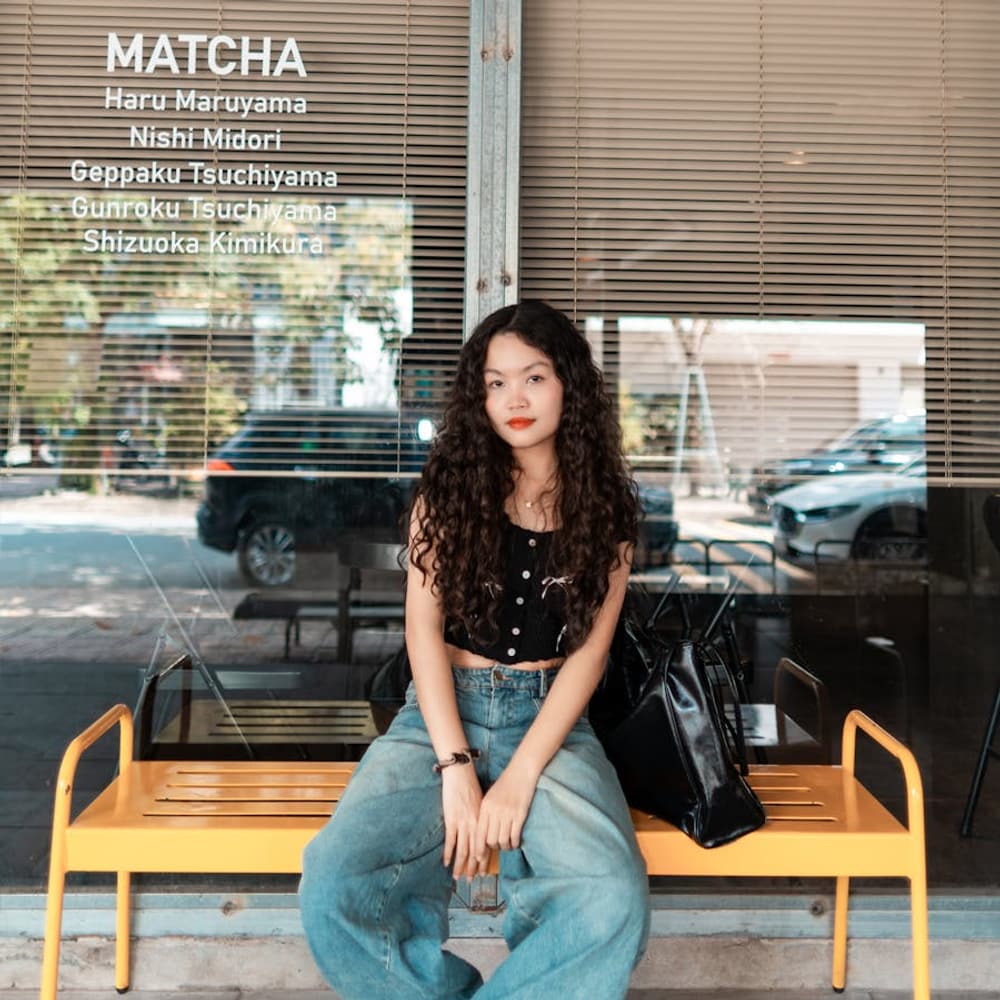 Young woman relaxing on an outdoor bench outside a city coffee shop on a neighborhood street