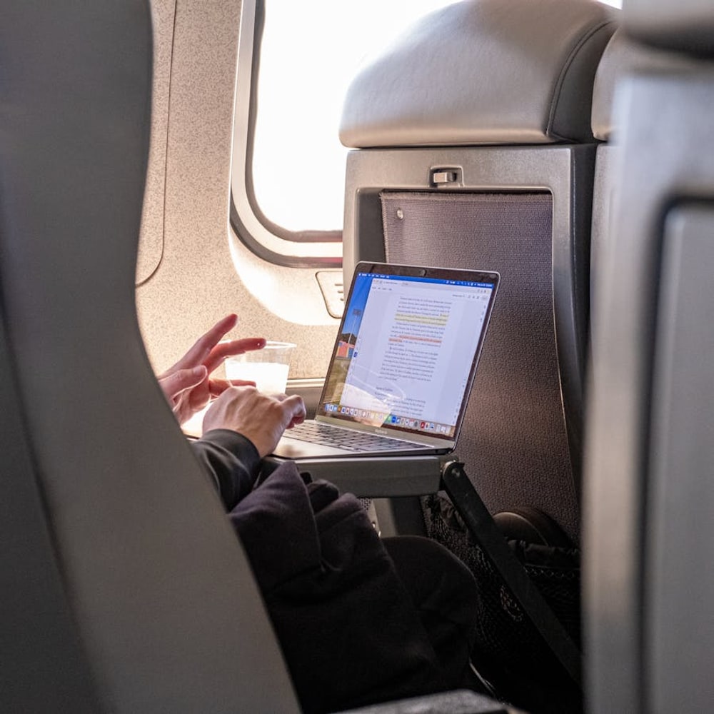 Traveler wearing headphones while working on a laptop during a flight