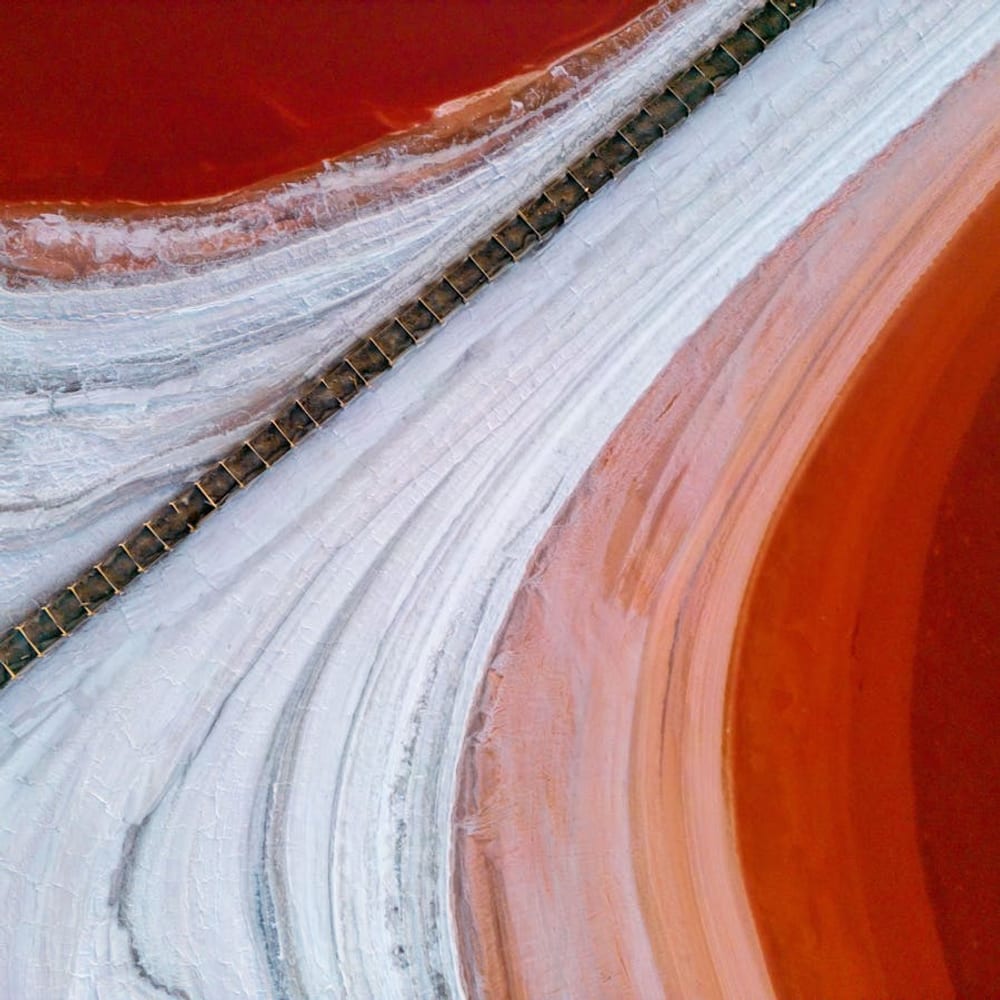 Aerial view of a vivid pink salt lake with a road cutting across otherworldly terrain