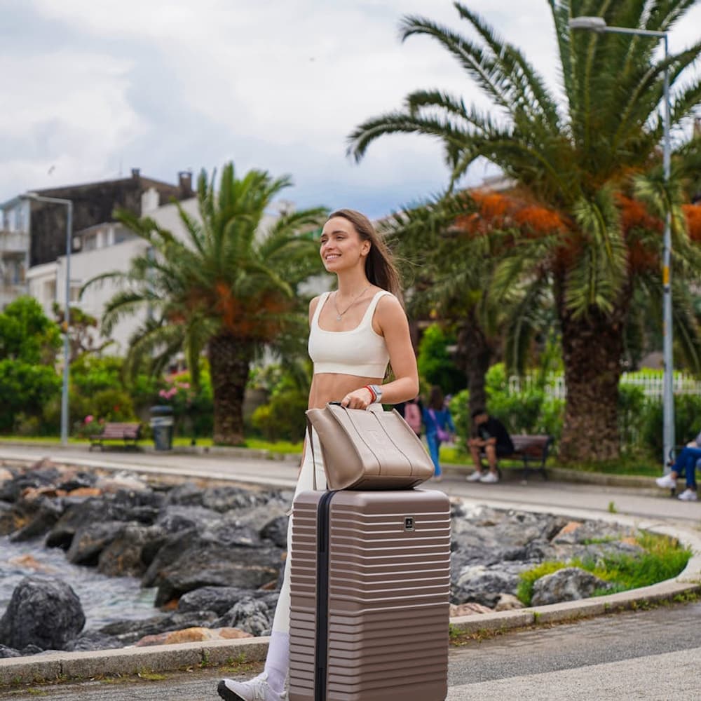 Solo traveler walking on a sidewalk while pulling a wheeled suitcase through an urban area