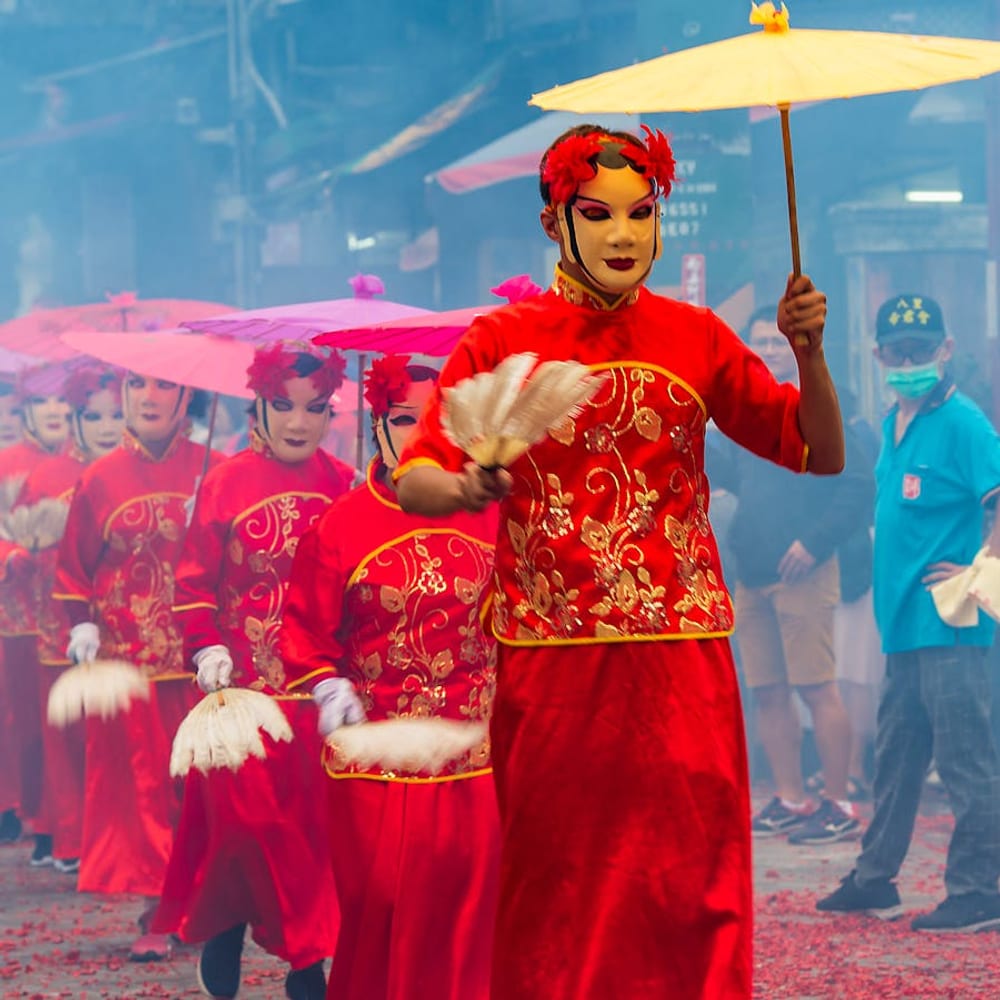 Festival parade with dancers in red traditional costumes and masks holding umbrellas