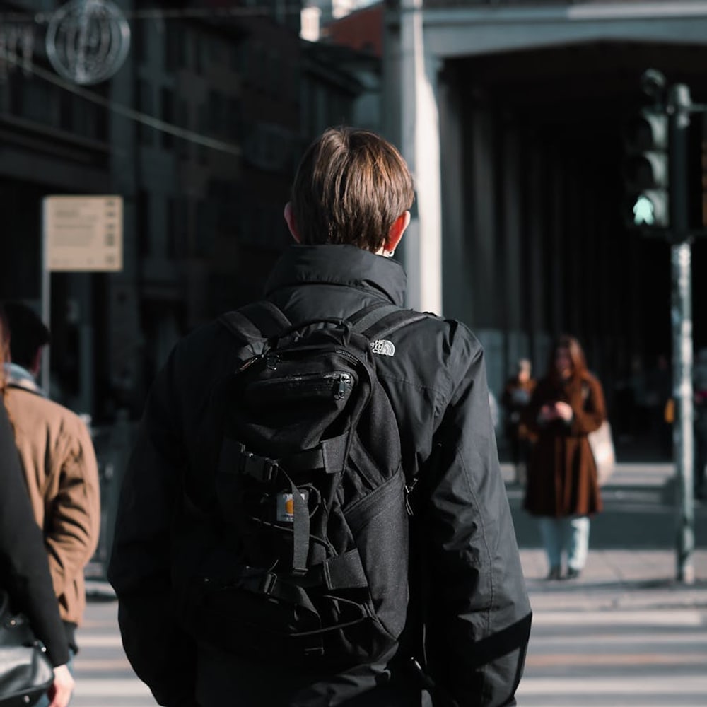 Traveler in a lightweight jacket with backpack standing at a city crosswalk