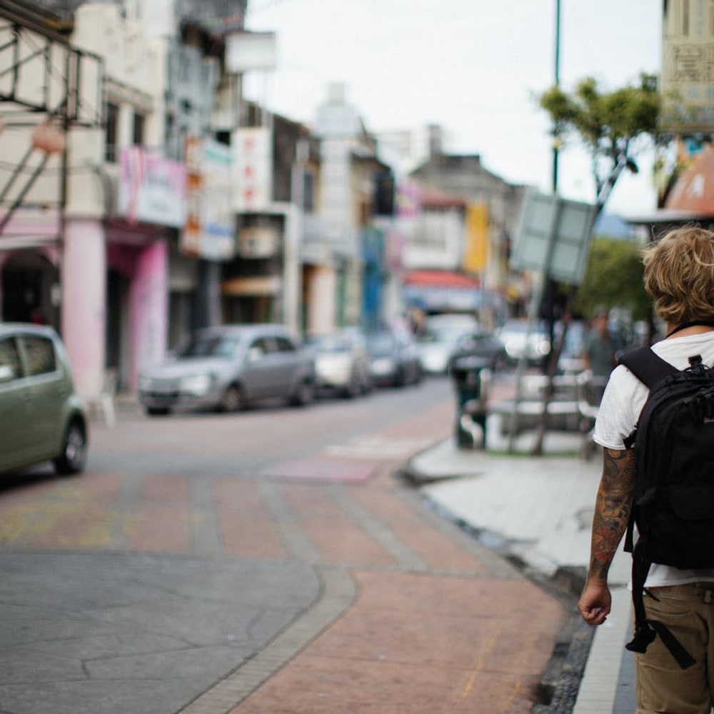 Back view of a solo traveler with backpack standing on an urban sidewalk
