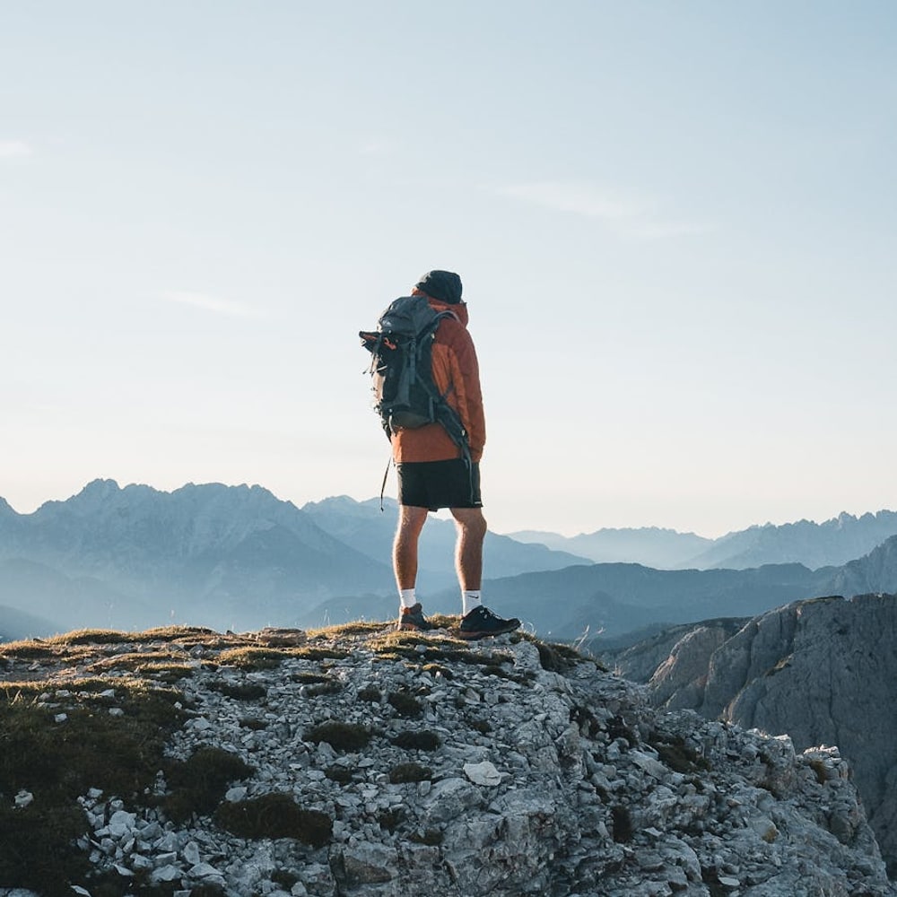 Solo traveler with backpack standing on a mountain summit overlooking a vast landscape
